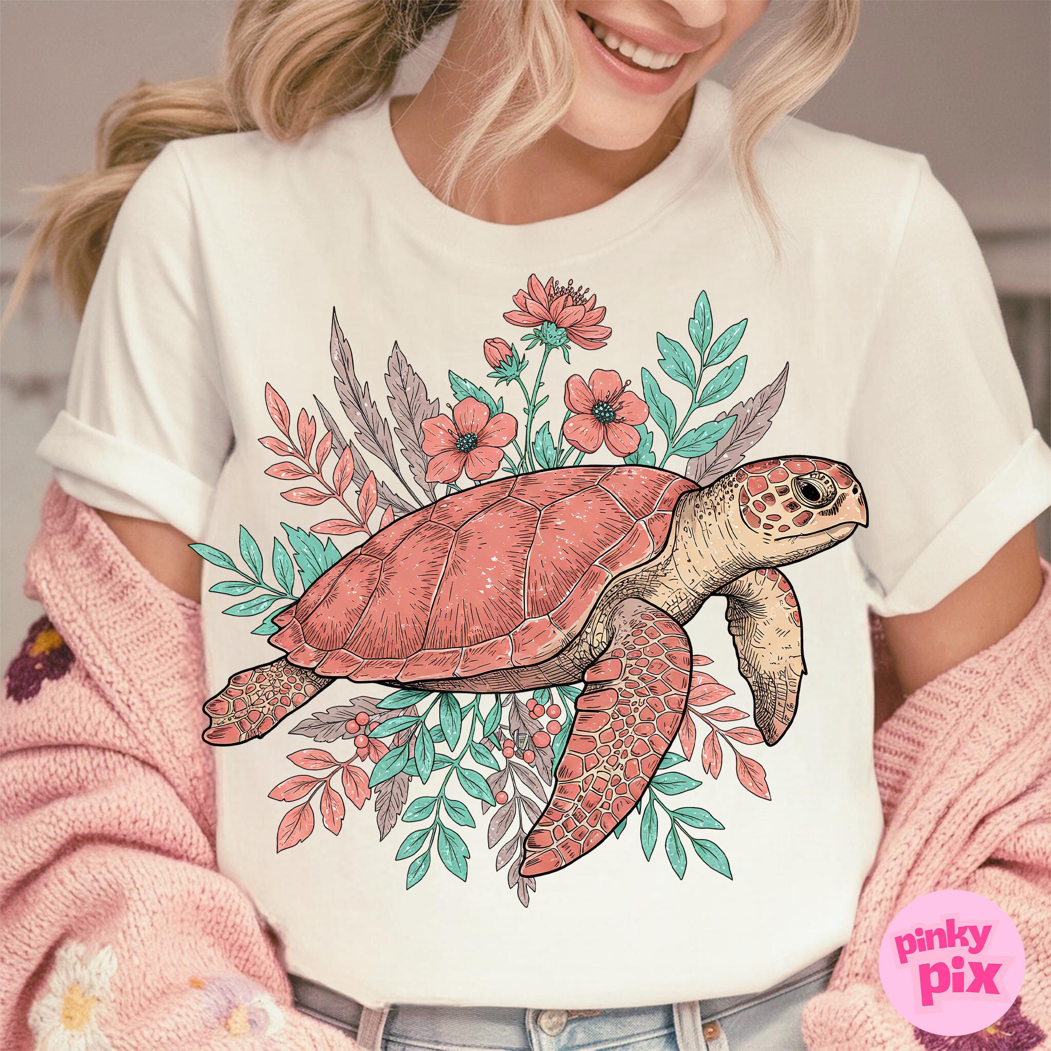 May include: White t-shirt with a pink and green floral design featuring a sea turtle. The turtle is outlined in black and has a pink shell.
