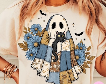 Pode incluir: Camiseta creme com um design de fantasma segurando um gato preto. O fantasma tem um padrão de colcha de retalhos. Flores azuis e folhas marrons cercam o fantasma. Morcegos e estrelas pretas também estão incluídos. A camiseta tem decote redondo e mangas curtas.