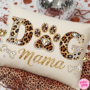 May include: Cream-colored rectangular pillow with the words "Dog Mama" in gold script and leopard print letters. The paw print and letters are embellished with rhinestones. Decorative dog bone accents are also included.