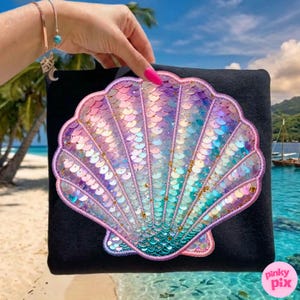 Puede incluir: Bolso tote negro con un gran diseño de concha iridiscente. La concha está hecha de lentejuelas en tonos rosa, morado y turquesa, con detalles dorados. El bolso se sostiene contra un fondo de playa tropical.