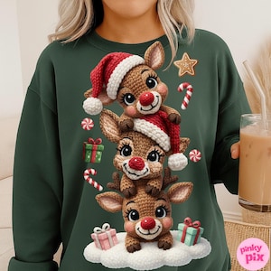 Puede incluir: Una sudadera verde oscuro con un diseño de tres renos de dibujos animados apilados, con narices rojas, gorros y bufandas de Papá Noel. La imagen incluye decoraciones navideñas como bastones de caramelo, regalos y galletas de jengibre.