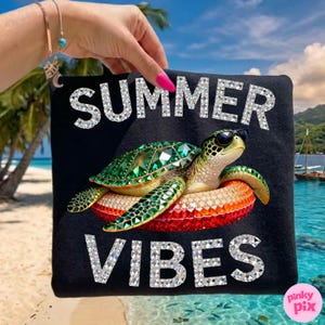 May include: Black tote bag with the words "SUMMER VIBES" in silver glitter. A bejeweled green sea turtle wearing sunglasses floats on an orange and red inflatable ring. The background shows a beach scene.