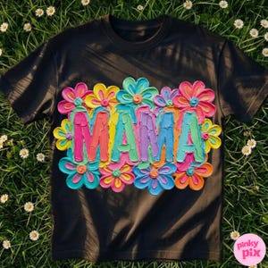May include: Black t-shirt with the word "MAMA" in colorful, textured letters, surrounded by vibrant, layered flower designs. The flowers feature shades of pink, yellow, blue, and orange, creating a cheerful and artistic look.