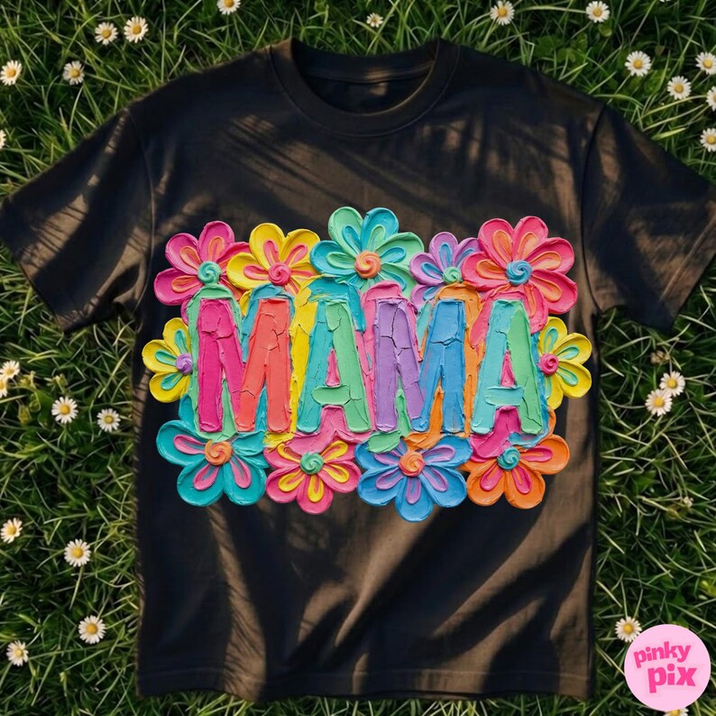 May include: Black t-shirt with the word "MAMA" in colorful, textured letters, surrounded by vibrant, layered flower designs. The flowers feature shades of pink, yellow, blue, and orange, creating a cheerful and artistic look.