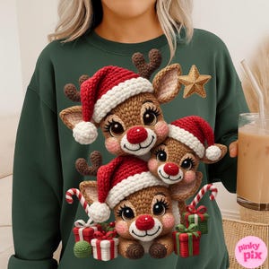 Puede incluir: Una sudadera verde oscuro con un diseño festivo de tres renos con gorros de Papá Noel rojos y blancos. Los renos tienen mejillas rosadas y narices rojas, con regalos y bastones de caramelo. También se ve una estrella dorada.