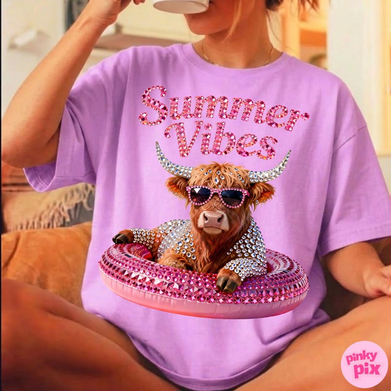 May include: A light purple t-shirt with the text "Summer Vibes" in pink rhinestone lettering. The shirt features a brown cow wearing sunglasses and a rhinestone-studded floatie. The cow is also adorned with rhinestones.