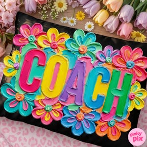 May include: Black pillow with the word "COACH" in colorful, textured lettering, surrounded by vibrant, painted flowers in shades of pink, yellow, blue, and orange. The pillow is decorated with a floral design.