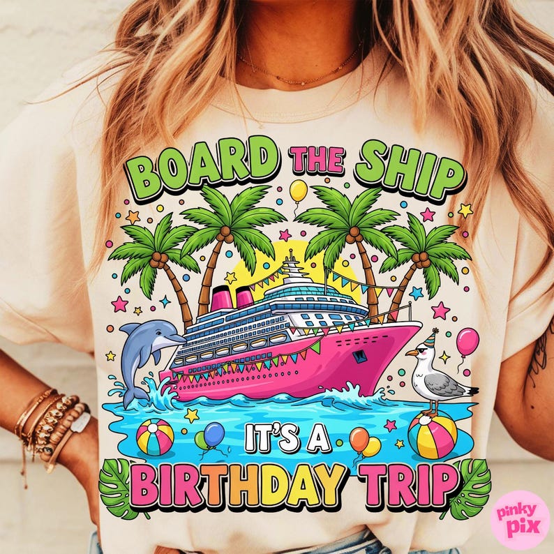 May include: A light beige t-shirt featuring a vibrant graphic of a pink cruise ship, palm trees, and a dolphin. Text says "BOARD THE SHIP" and "IT'S A BIRTHDAY TRIP". The design includes balloons, stars, and a seagull.