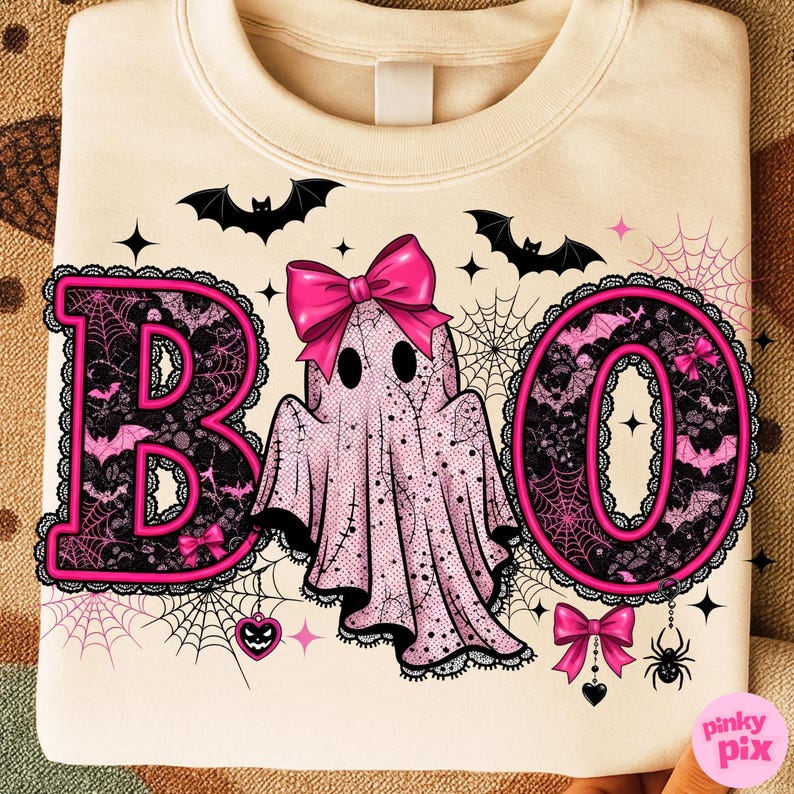 Puede incluir: Sudadera color crema con un dise&ntilde;o tem&aacute;tico de Halloween. La palabra "BOO" est&aacute; escrita en letras rosas con detalles de encaje negro y un lazo rosa. Un fantasma rosa con un lazo est&aacute; en el centro, rodeado de murci&eacute;lagos, telara&ntilde;as y una ara&ntilde;a.
