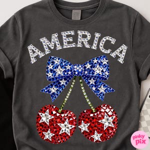May include: Dark gray crew neck sweatshirt with the word "AMERICA" in silver rhinestones. Below the text is a blue bow with white star rhinestones and red cherry rhinestones with white star rhinestones.