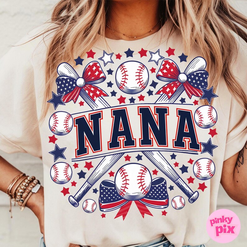 May include: A beige t-shirt with a graphic design featuring two crossed baseball bats, baseballs, red, white, and blue bows, and the word "NANA" in navy blue letters.
