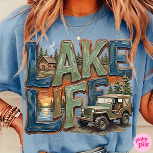 May include: A light blue t-shirt with the words "LAKE LIFE" in a textured, multi-colored design. The graphic includes a cabin, a sunset over a lake, and a green jeep.