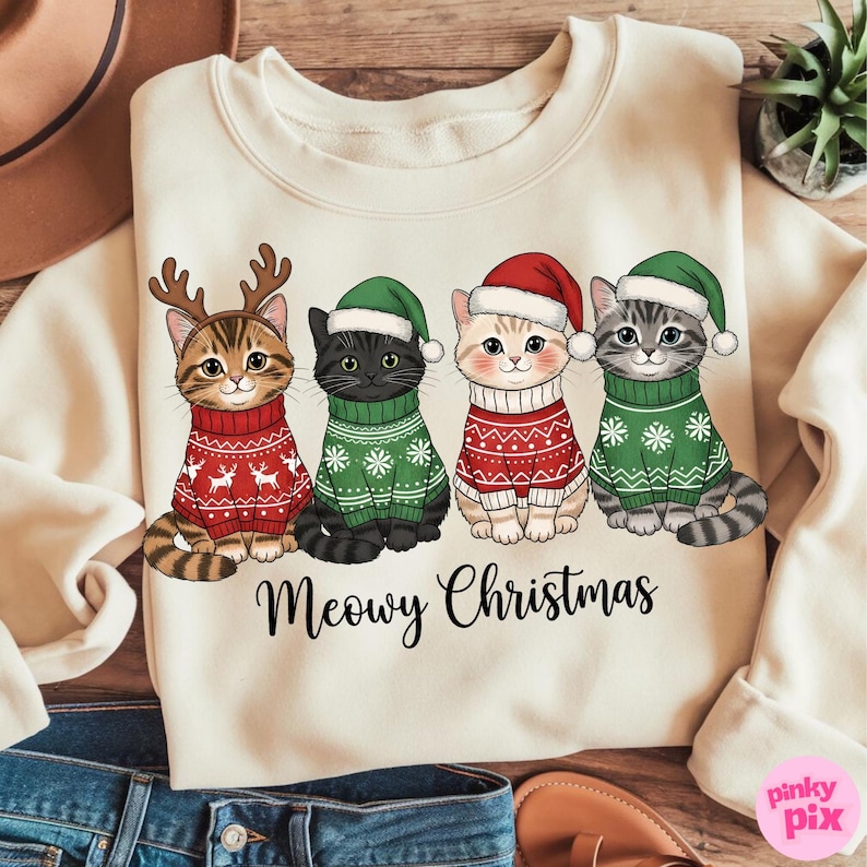 以下が含まれることがあります： クリスマスセーターと帽子をかぶった4匹の漫画の猫が特徴のクリーム色のスウェットシャツ。猫は、お祝いの模様の赤と緑のセーターを着ています。「Meowy Christmas」というテキストが猫の下に印刷されています。