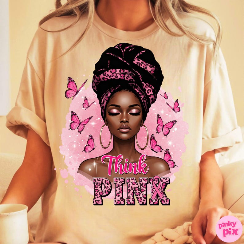 K&ouml;nnte beinhalten: Beiges T-Shirt mit einer Grafik einer schwarzen Frau mit einem schwarz-rosa Kopftuch, gro&szlig;en goldenen Creolen und rosa Schmetterlingen. Der Text "Think PINK" ist in Rosa mit einem rosa Band dargestellt.
