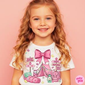 May include: A white t-shirt with a pink bow and a camping scene design. The design includes a tent, backpack, and lantern, with the text "Camp Cuties" and "Tent Sisters Girls Only" on signs. The illustration is in a cartoon style.