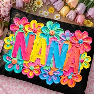 May include: Black decorative pillow with the word "NANA" in colorful, textured letters. The letters are surrounded by vibrant, multi-colored flowers in shades of pink, yellow, blue, and green. The pillow is a decorative home accent.