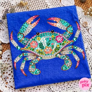 May include: A blue square featuring a bejeweled crab design. The crab is decorated with colorful rhinestones in shades of teal, pink, and clear, with floral accents. The crab's claws and legs are also adorned with rhinestones. The image has the text "pinky pix" in the bottom right corner.