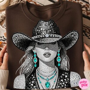 May include: A brown sweatshirt featuring a detailed illustration of a woman wearing a bedazzled cowboy hat and jewelry. The artwork is in grayscale with accents of turquoise. The design includes a necklace, earrings, and a vest.