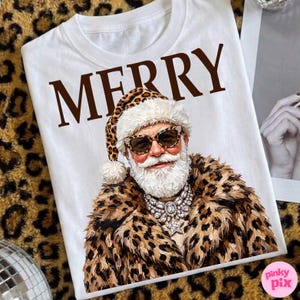 以下が含まれることがあります： 白いTシャツに茶色の文字でMERRYと書かれ、その下にヒョウ柄の帽子、ヒョウ柄のコート、大きなサングラス、星型のペンダントが付いた大ぶりのシルバーのステートメントネックレスを身に着けた、白いひげの人物のグラフィックがプリントされています。