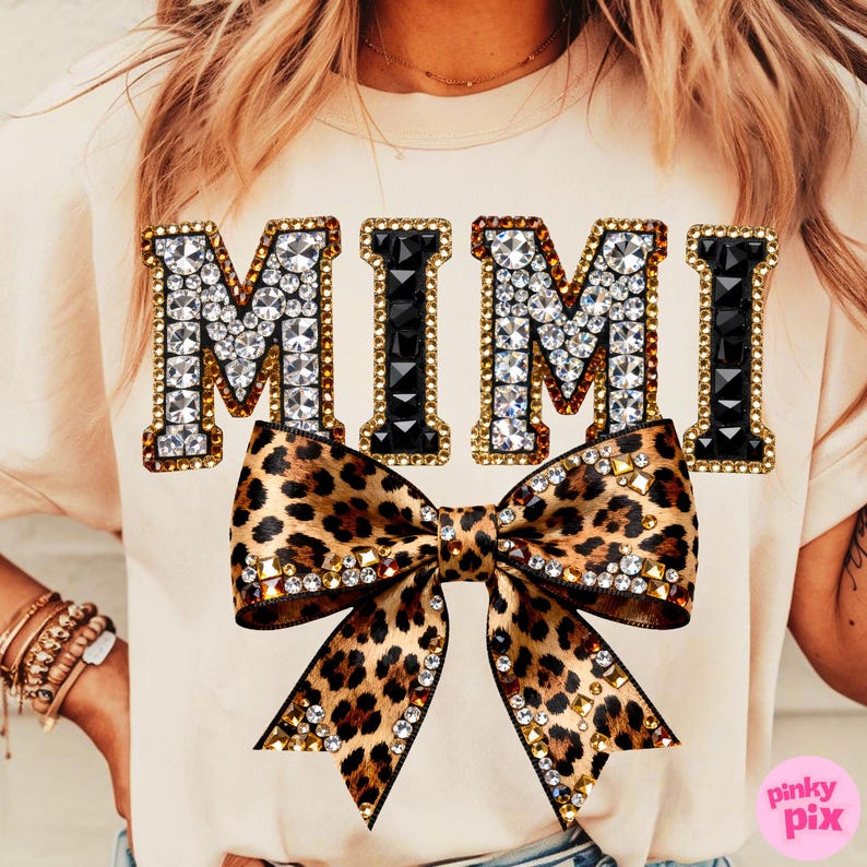 May include: Cream-colored t-shirt with the word "MIMI" in jeweled letters. A leopard print bow with crystal and gold accents is centered below the text. The shirt has short sleeves.
