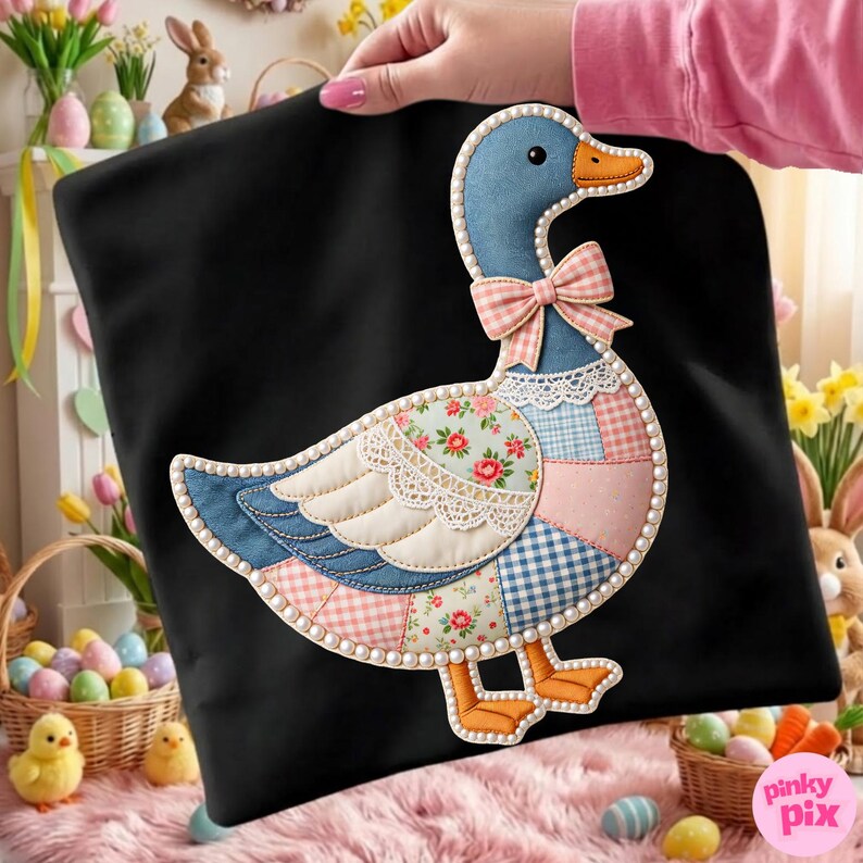 K&ouml;nnte beinhalten: Schwarzes Kissen mit einem Patchwork-Enten-Design. Die Ente hat einen blauen Kopf, einen orangefarbenen Schnabel und F&uuml;&szlig;e sowie eine rosa Schleife. Der K&ouml;rper besteht aus verschiedenen gemusterten Stoffen, darunter Blumen und Vichy, und ist mit Perlen umrandet.