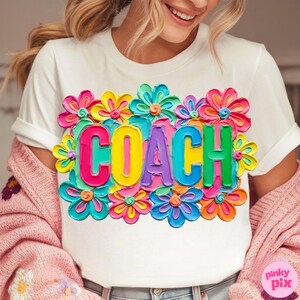 May include: White t-shirt with the word "COACH" in colorful, 3D-style letters, surrounded by vibrant, multi-colored flowers. The design is eye-catching and bold, perfect for a coach.
