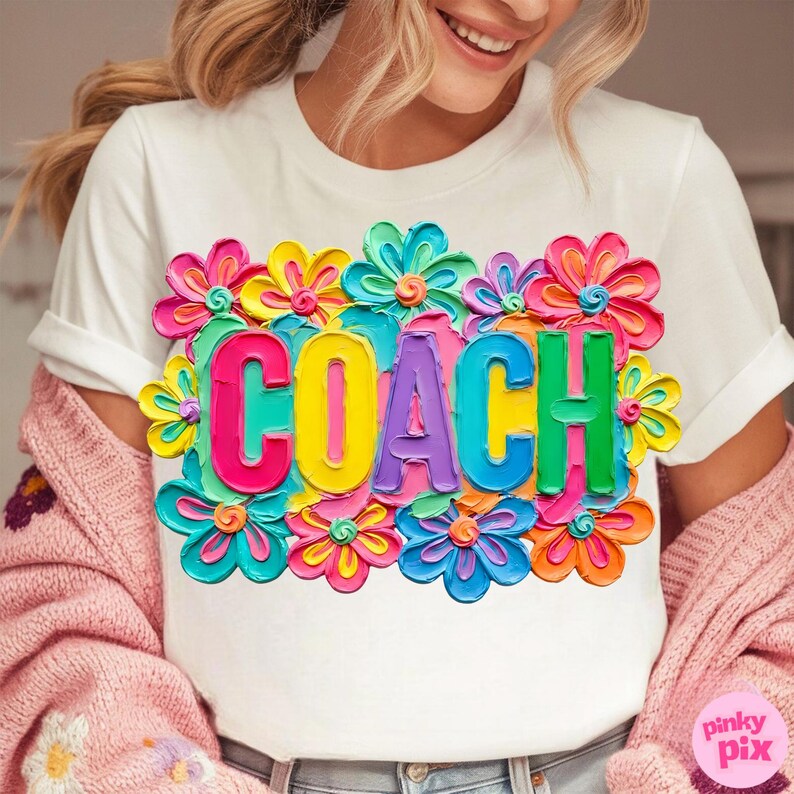 May include: White t-shirt with the word "COACH" in colorful, 3D-style letters, surrounded by vibrant, multi-colored flowers. The design is eye-catching and bold, perfect for a coach.