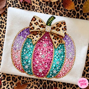 Op de afbeelding: Een pompoenvormige decoratie bedekt met veelkleurige strass-steentjes, met verticale segmenten in roze, talingblauw en lichtpaars. De pompoen is versierd met zilveren sterren en bekroond met een strik met luipaardprint en een groene steel.
