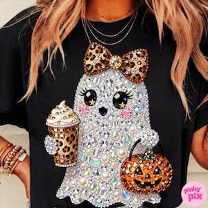 May include: A black t-shirt featuring a graphic of a ghost adorned with clear, iridescent, and pearl-like rhinestones. The ghost wears a leopard print bow, holds a leopard print coffee cup, and carries a jack-o'-lantern bucket with orange gems.