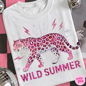 May include: White t-shirt featuring a pink leopard design with crystal accents and the text "WILD SUMMER". The leopard is surrounded by pink lightning bolts and stars.