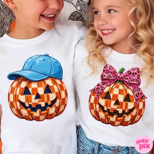 May include: Two white t-shirts featuring graphic prints of orange and white checkered pumpkins. The left pumpkin wears a blue baseball cap, while the right pumpkin is adorned with a pink leopard print bow. Both pumpkins have carved faces.
