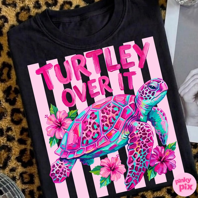 May include: Black t-shirt with a vibrant graphic of a sea turtle, featuring pink, teal, and leopard print details. The text "TURTLEY OVER IT" is displayed above the turtle, set against a pink and white striped background.