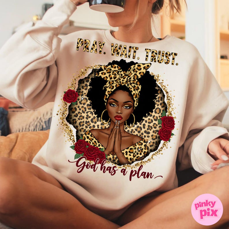 May include: A cream-colored sweatshirt with a graphic print of a Black woman with a leopard print headscarf and a gold glitter background. The text "Pray. Wait. Trust. God has a plan." is printed on the sweatshirt.