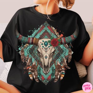 May include: Black t-shirt with a detailed graphic of a bull skull. The design incorporates turquoise, red, and brown tribal patterns, feathers, a red rose, and dream catchers, creating a bohemian aesthetic.