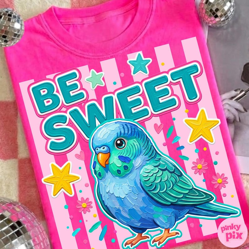 May include: A pink t-shirt with the words "BE SWEET" in teal and white, featuring a blue and green parakeet illustration. The design includes stars, flowers, and sprinkles.