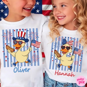 May include: White t-shirts with a patriotic design featuring cartoon ducks holding hot dogs and American flags. The ducks wear heart-shaped sunglasses and festive hats. The names "Oliver" and "Hannah" are printed in blue and red cursive.