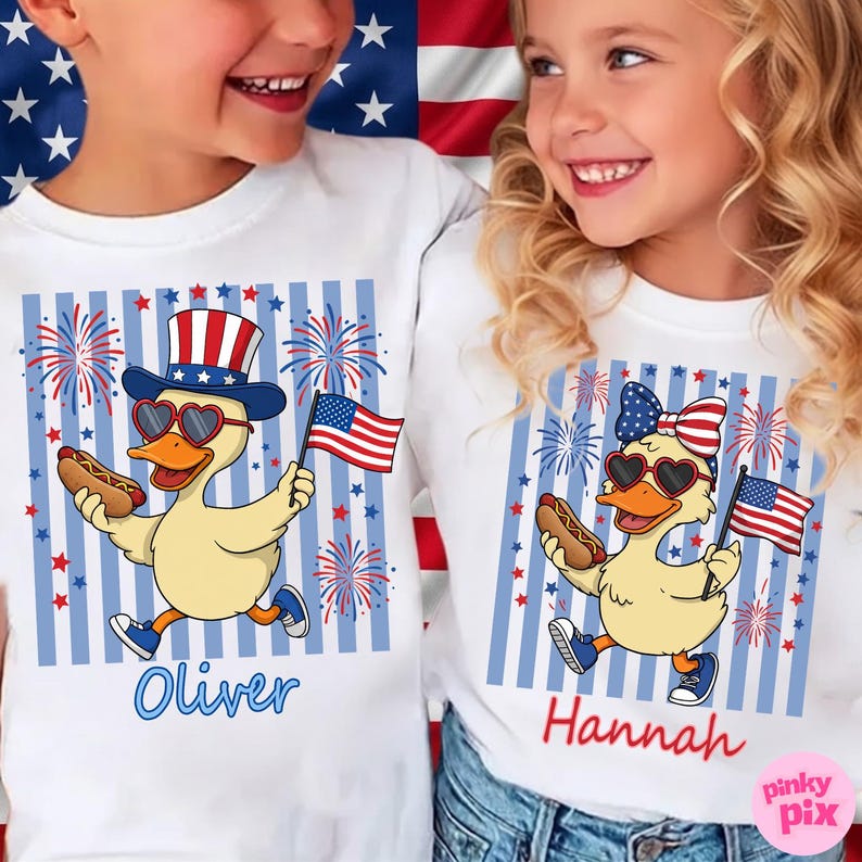 May include: White t-shirts with a patriotic design featuring cartoon ducks holding hot dogs and American flags. The ducks wear heart-shaped sunglasses and festive hats. The names "Oliver" and "Hannah" are printed in blue and red cursive.