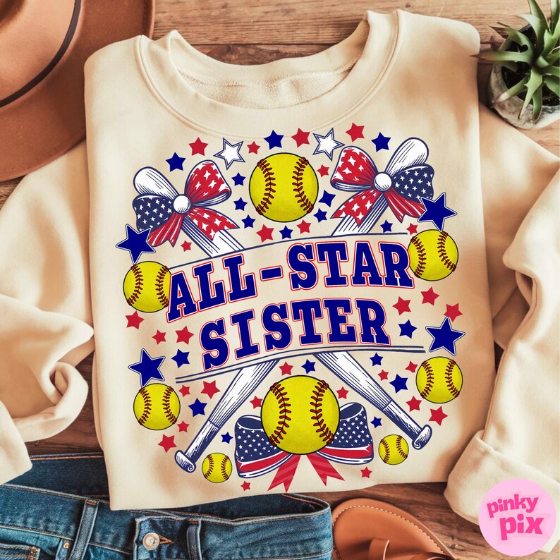 May include: Cream-colored sweatshirt with a softball-themed design. The design includes yellow softballs, crossed baseball bats, red and blue stars, and the text "ALL-STAR SISTER" in blue. Patriotic bows complete the design.