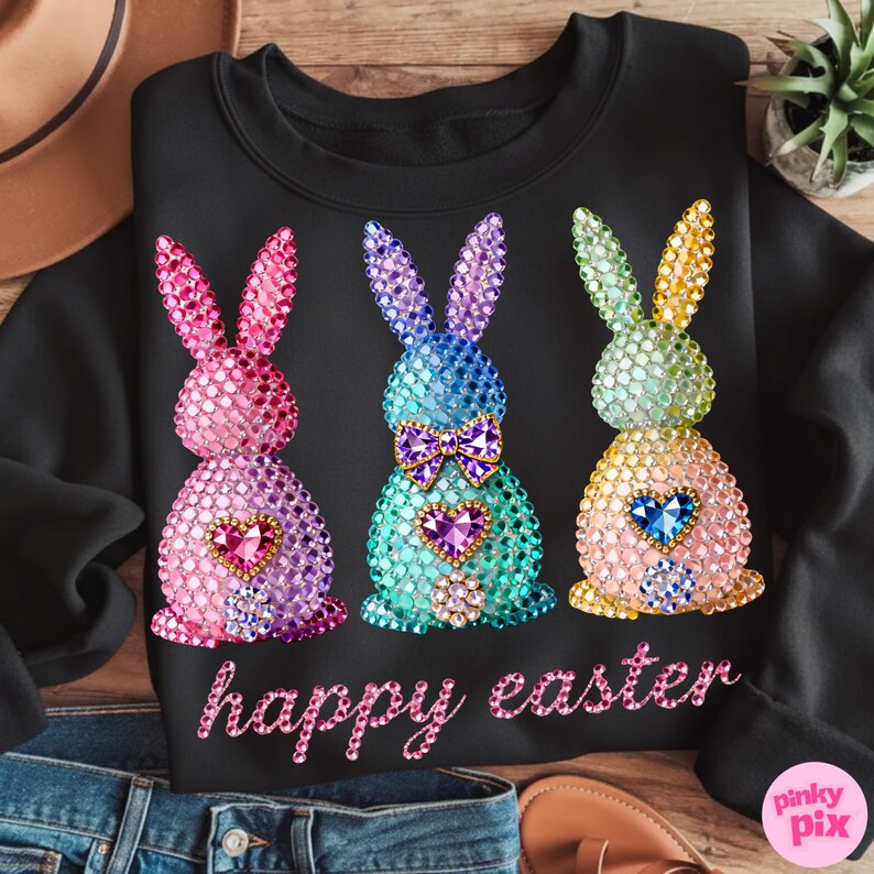 May include: Black sweatshirt featuring three jeweled Easter bunnies in pink, blue, and yellow. Each bunny has a heart-shaped gem and a bow tie. The words "happy easter" are written in pink script below the bunnies.