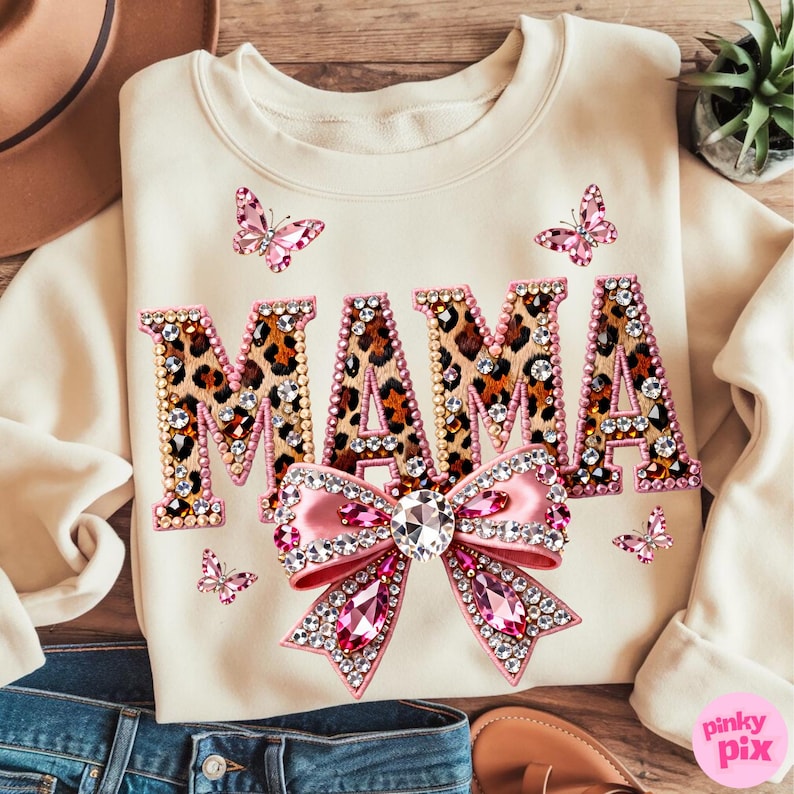 May include: Cream-colored sweatshirt with the word "MAMA" in leopard print letters, embellished with rhinestones. A pink bow and several pink butterfly accents complete the design. The sweatshirt is a casual, stylish garment.