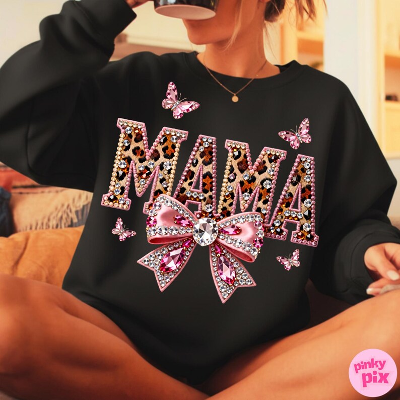 May include: Black sweatshirt with the word "MAMA" in leopard print letters, embellished with rhinestones. A large pink bow with a crystal center and pink rhinestone accents is below the word. Pink butterflies are scattered around the design.