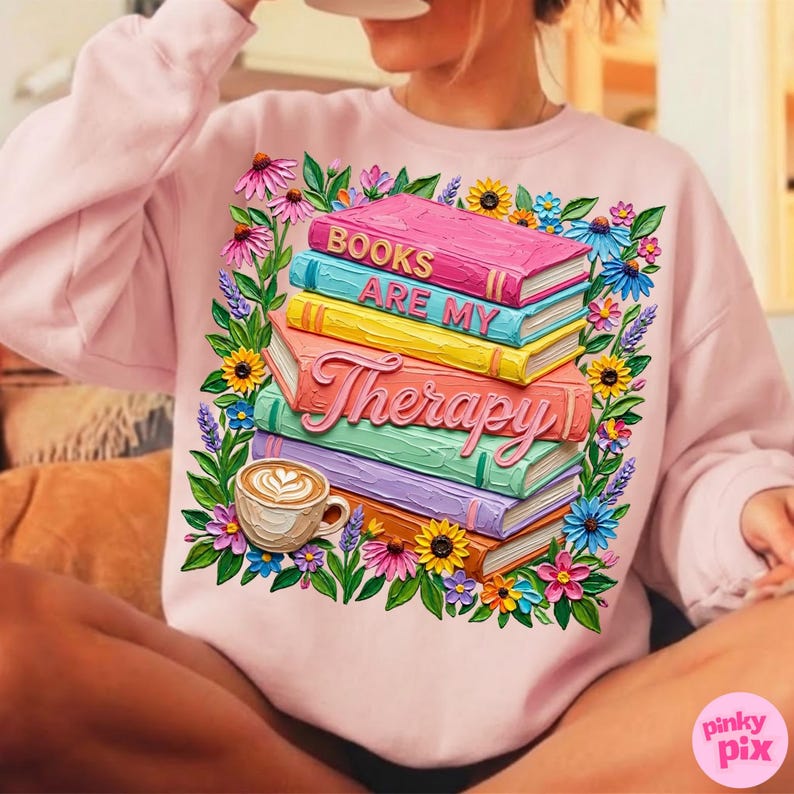 May include: A light pink sweatshirt featuring a stack of colorful books with the words "BOOKS ARE MY Therapy". The design includes a floral wreath and a coffee cup. The sweatshirt is a comfortable, casual style.