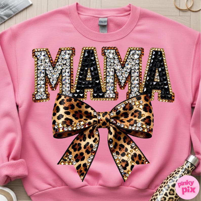 May include: Pink sweatshirt with the word "MAMA" in rhinestone and black gem lettering, outlined in gold. A large leopard print bow with rhinestone accents is centered below the word. The sweatshirt is a crew neck style.