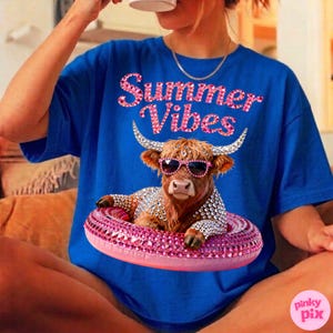 May include: Royal blue t-shirt with the text "Summer Vibes" in pink rhinestone lettering. The shirt features a graphic of a brown cow wearing sunglasses and a rhinestone-studded life preserver.