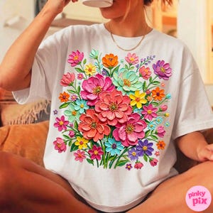 May include: White t-shirt featuring a vibrant floral bouquet design. The bouquet includes pink, orange, yellow, blue, and purple flowers. The flowers have a 3D effect, creating a textured appearance. The shirt is a casual style.
