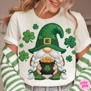 May include: White t-shirt featuring a St. Patrick's Day gnome design. The gnome wears a green hat with shamrocks and a gold buckle, holding a pot of gold coins. Green shamrocks are scattered around the gnome.
