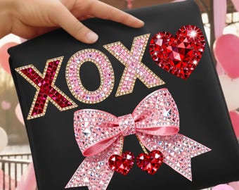 May include: Black clutch with rhinestone embellishments spelling "XOX" and featuring a pink bow and red hearts. The letters and bow are encrusted with pink rhinestones, and the hearts are red.