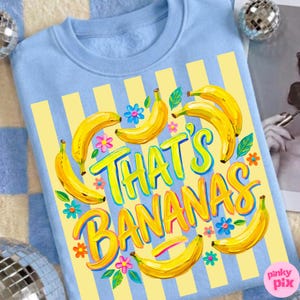 Pu&ograve; includere: Felpa azzurra con un design a righe gialle e blu. La felpa presenta la frase "THAT'S BANANAS" in giallo e blu, circondata da illustrazioni di banane gialle e fiori colorati.