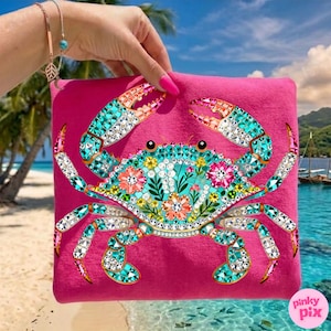 May include: A hot pink tote bag featuring a detailed crab design. The crab is embellished with turquoise, orange, and clear rhinestones, and floral accents. The background shows a tropical beach scene.