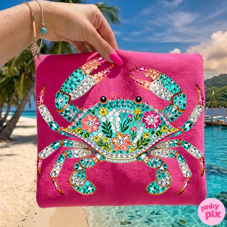 May include: A hot pink tote bag featuring a detailed crab design. The crab is embellished with turquoise, orange, and clear rhinestones, and floral accents. The background shows a tropical beach scene.